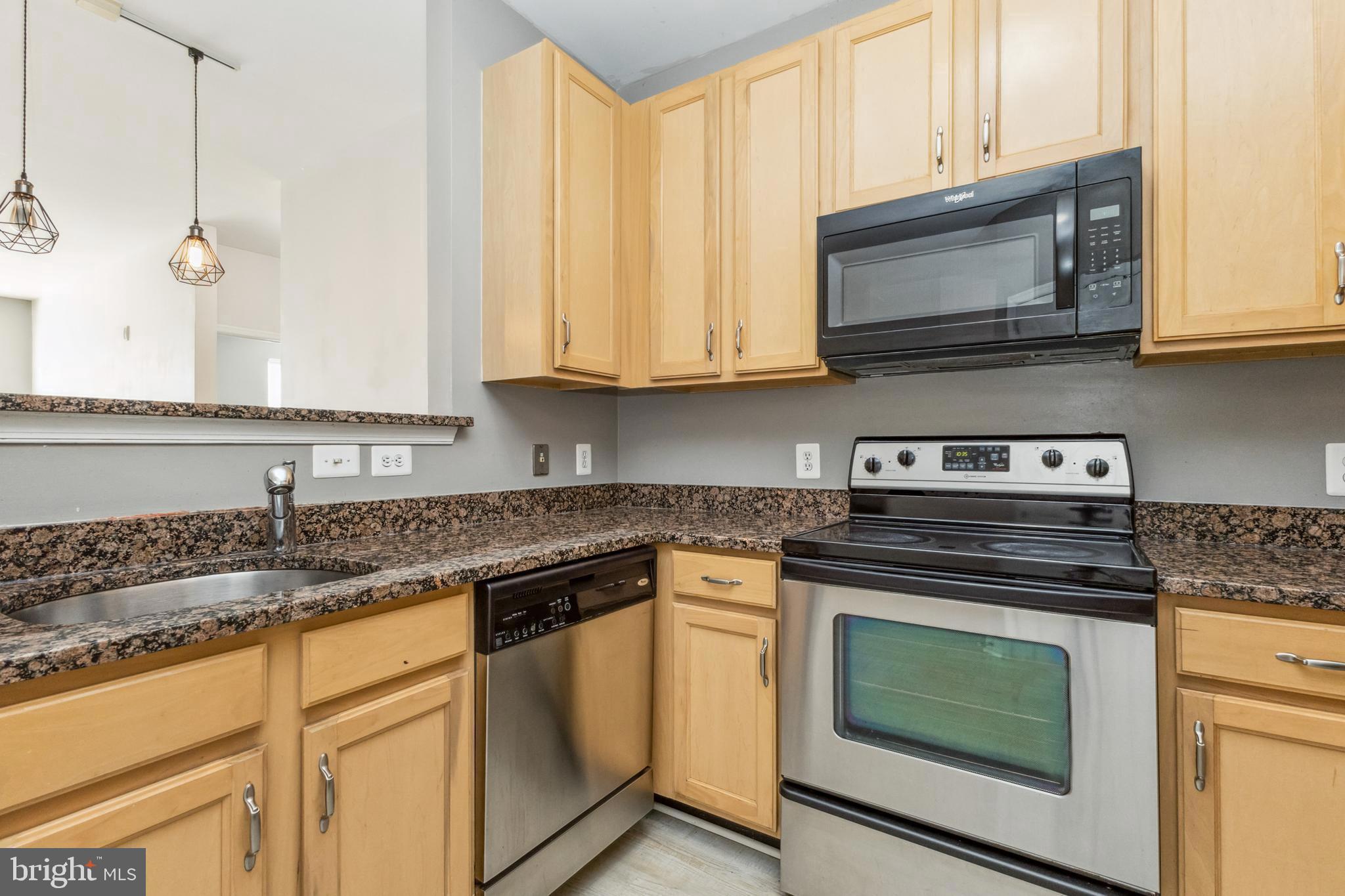 22664 Blue Elder Terrace, Unit 102 Brambleton, VA 20148 - Photo 9 of 25 a kitchen with granite countertop white cabinets and a stove a oven with wooden floor
