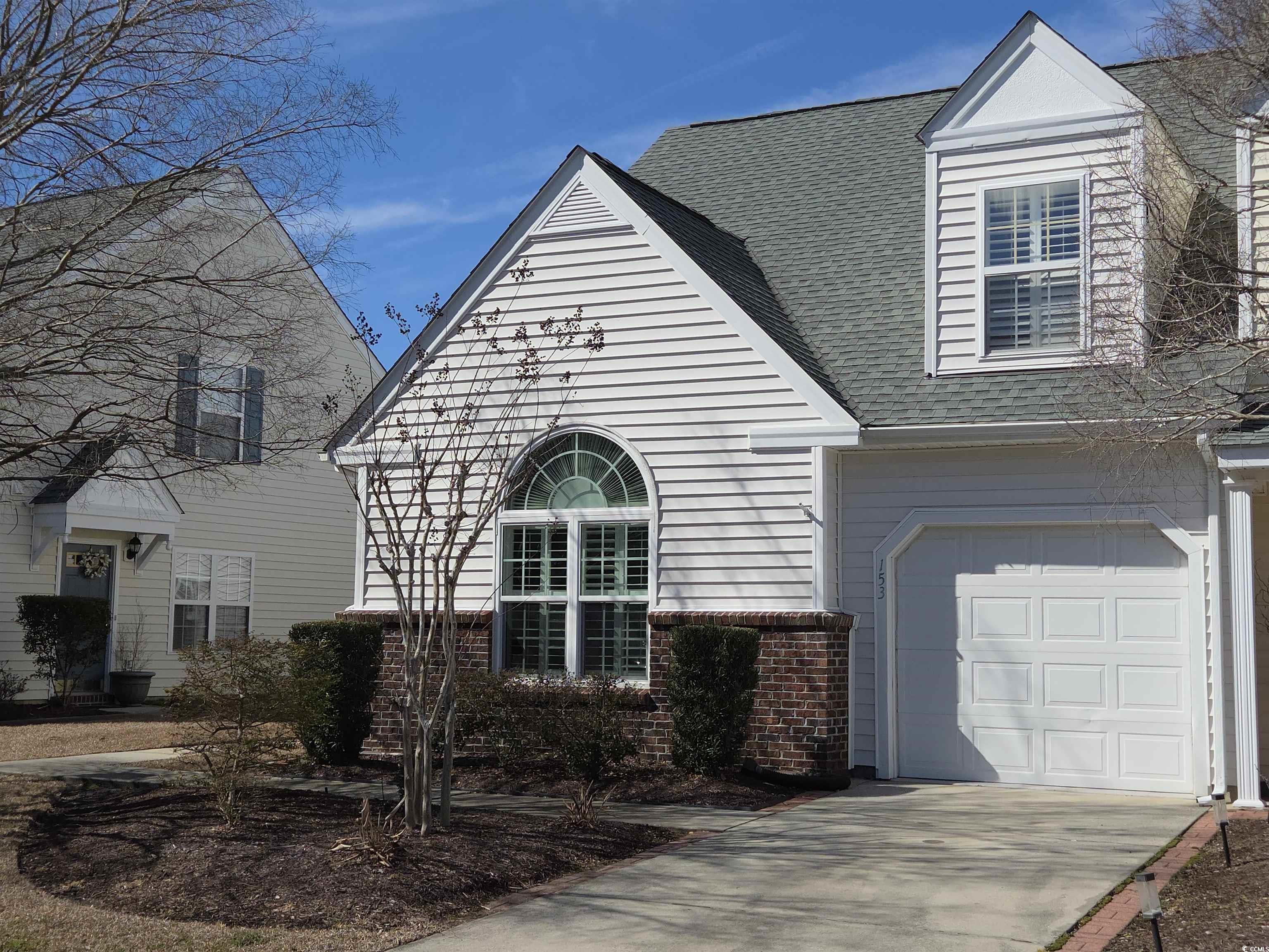 Traditional-style house featuring roof with shingles, brick siding, driveway, a garage, and covered porch