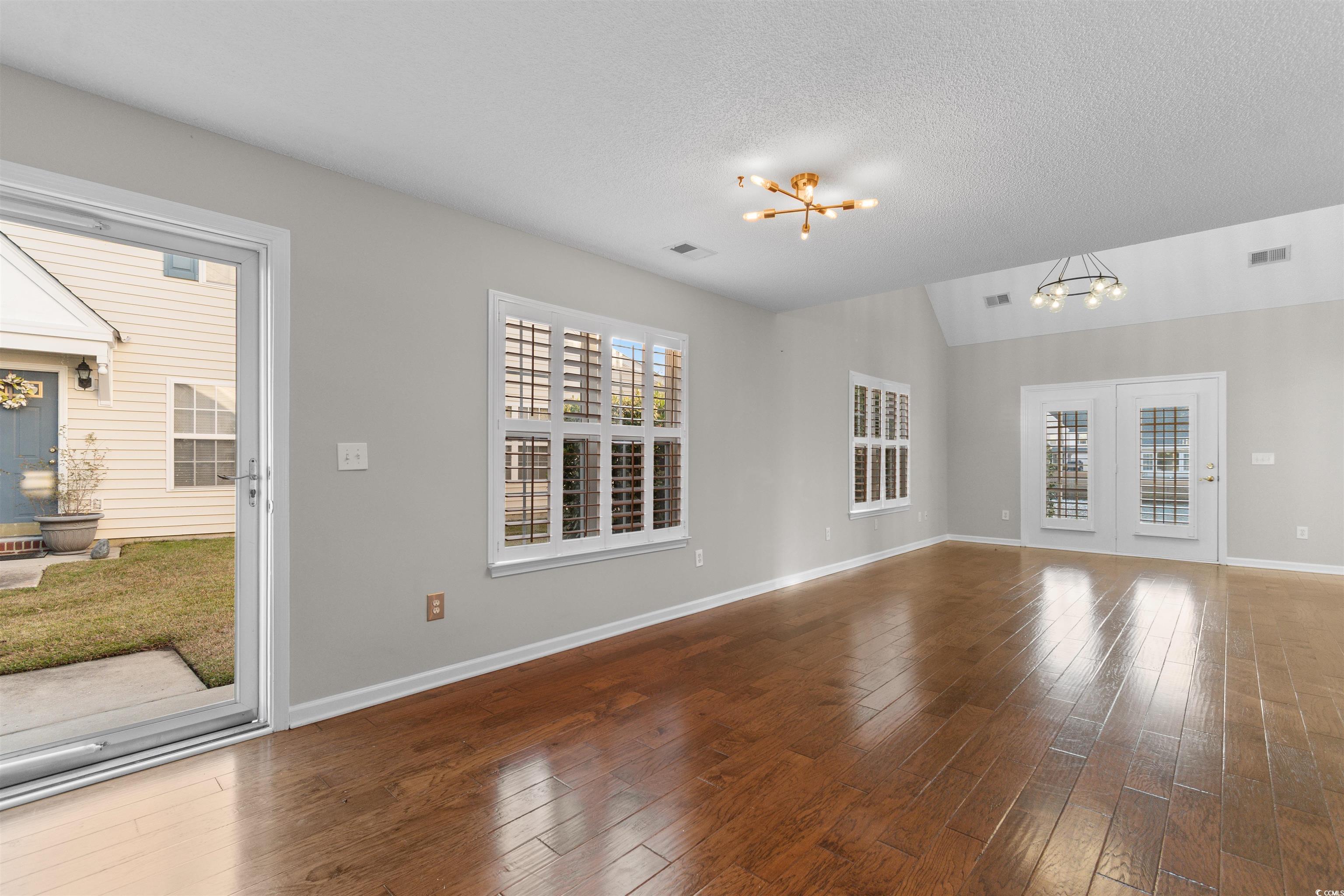 153 Wimbledon Way, Unit 153 Murrells Inlet, SC 29576 - Photo 11 of 32 Unfurnished living room with a chandelier, healthy amount of natural light, hardwood / wood-style flooring, lofted ceiling, and a textured ceiling