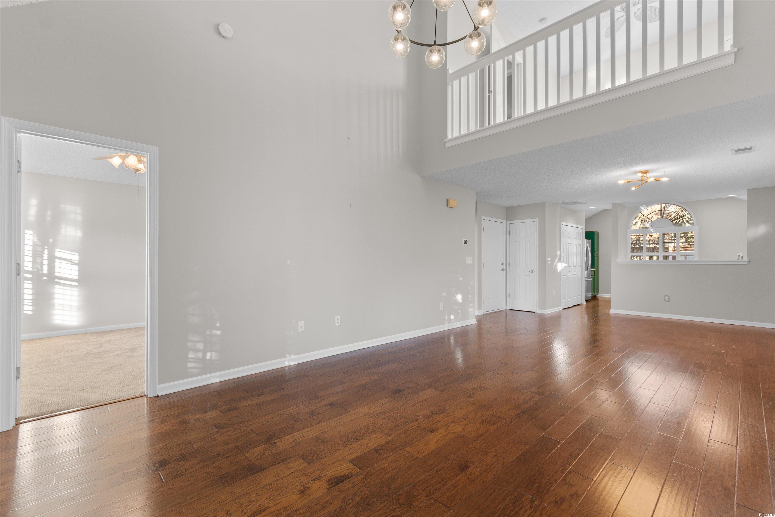 153 Wimbledon Way, Unit 153 Murrells Inlet, SC 29576 - Photo 14 of 32 Unfurnished living room featuring a chandelier, dark wood-style flooring, and a towering ceiling