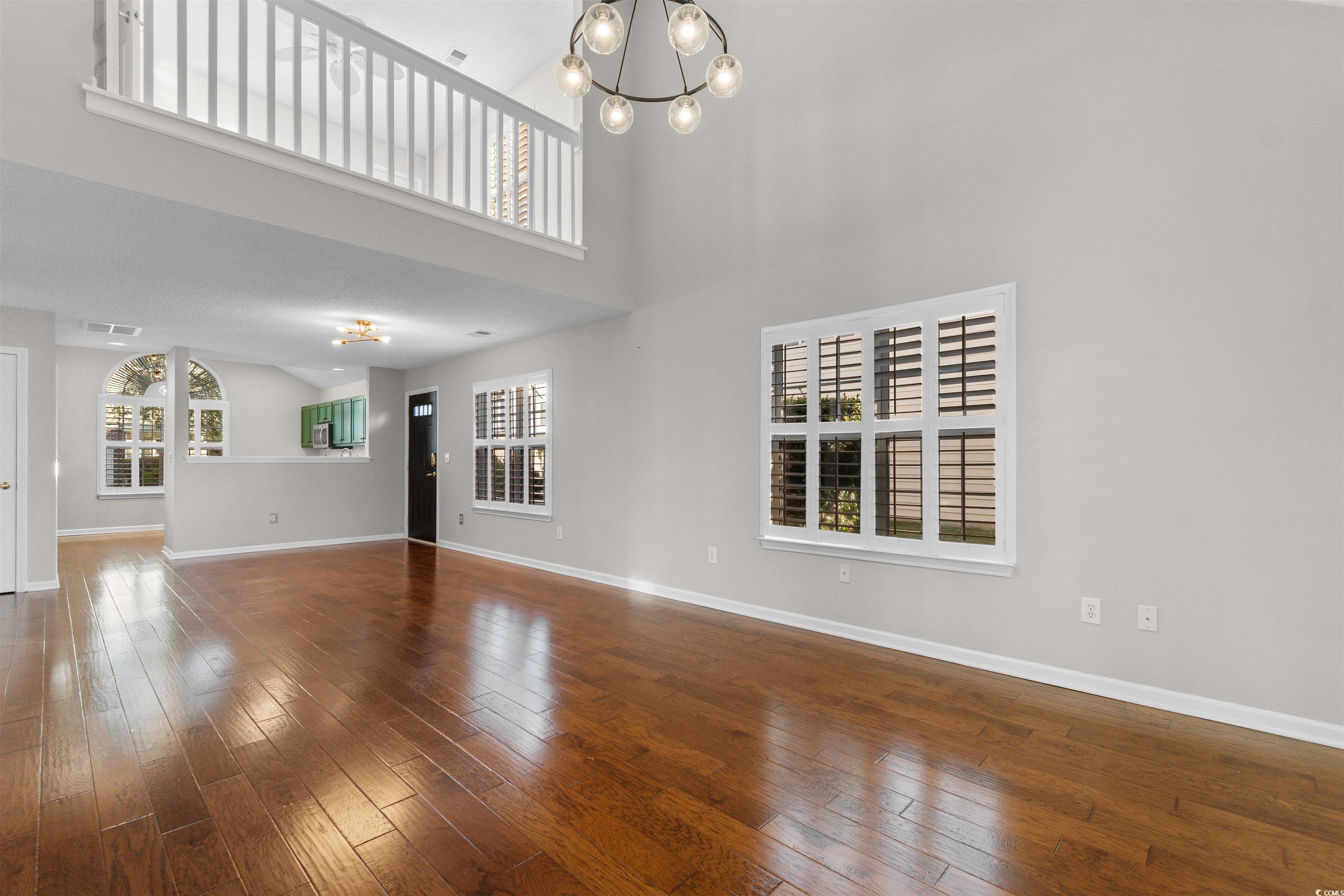 153 Wimbledon Way, Unit 153 Murrells Inlet, SC 29576 - Photo 9 of 32 Unfurnished living room featuring a chandelier, dark wood finished floors, plenty of natural light, and a high ceiling