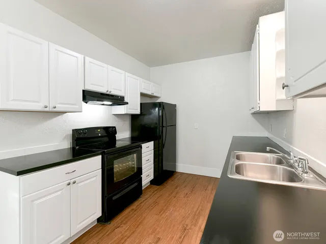 a kitchen with stainless steel appliances granite countertop a sink a stove a refrigerator with grey cabinets and wooden floor