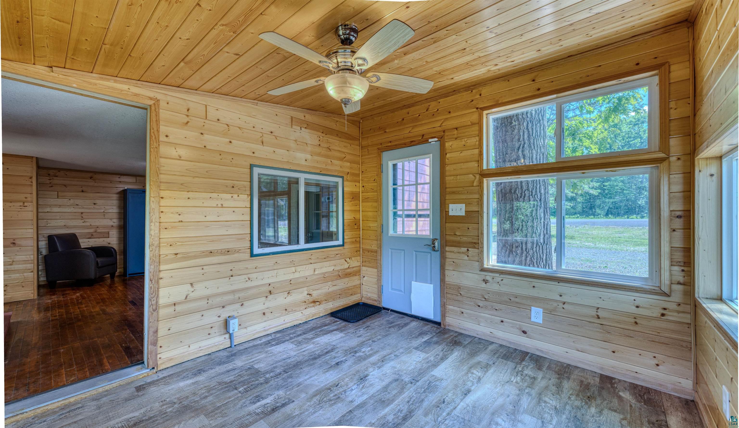 66075 Rooster Road Iron River, WI 54847 - Photo 15 of 52 Wood-paneled room featuring a ceiling fan with integrated lighting, wood-finish flooring, multiple windows, and a panel door with a window