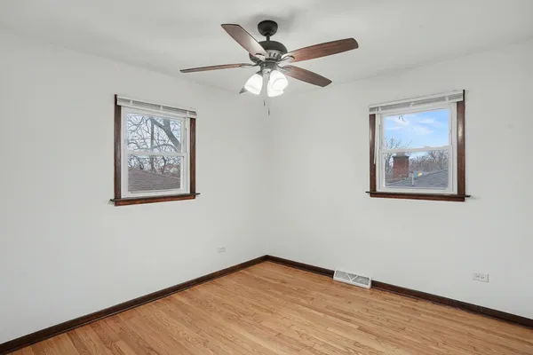 a view of an empty room with wooden floor and a ceiling fan