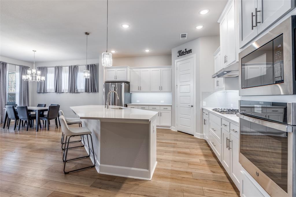 356 Greenbriar Road Little Elm, TX 75068 - Photo 10 of 25 Kitchen with stainless steel appliances, white cabinets, a center island with sink, light wood finished floors, and a kitchen breakfast bar