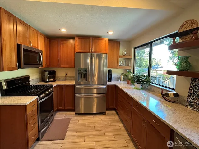 a kitchen with stainless steel appliances granite countertop a refrigerator a sink dishwasher a stove top oven and a dining table with wooden floor