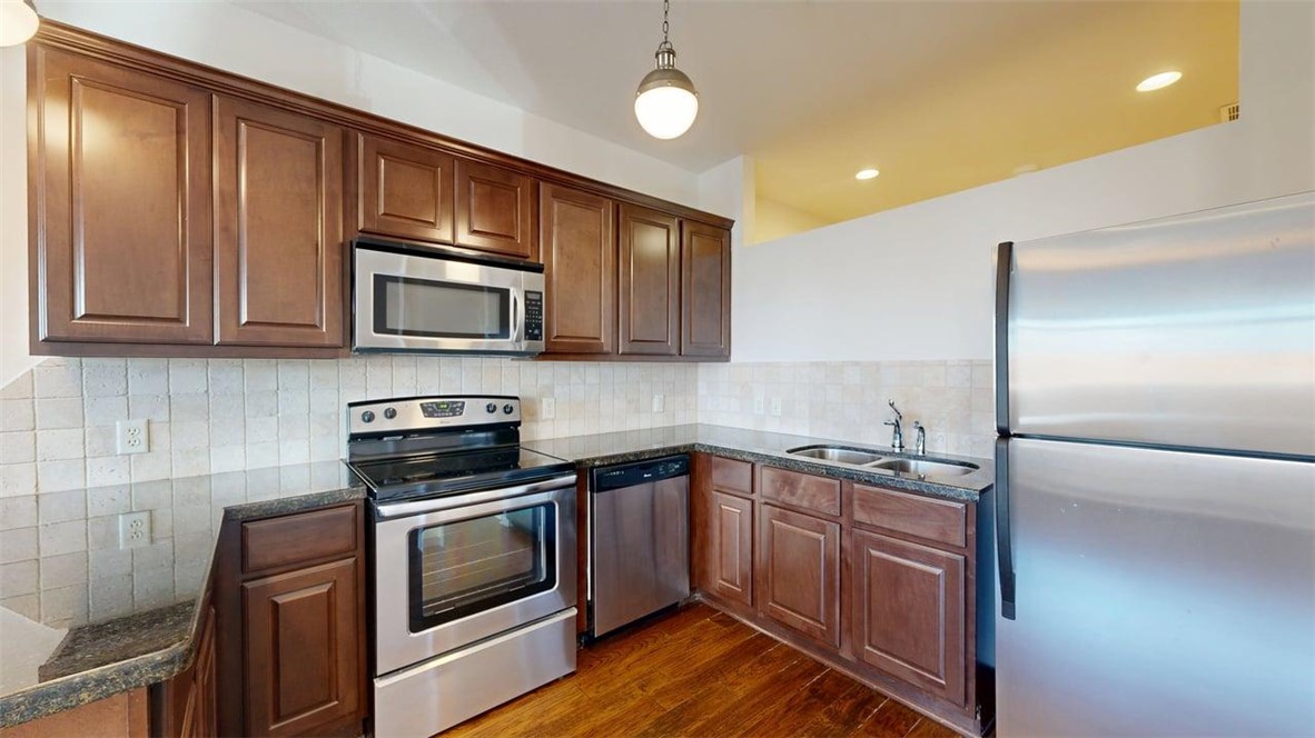 206 North Main Street, Unit 124 Bryan, TX 77803 - Photo 8 of 17 a kitchen with stainless steel appliances granite countertop wooden cabinets a stove a sink and dishwasher a refrigerator with wooden floor