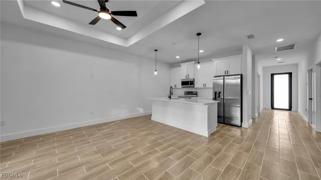 a large white kitchen with stainless steel appliances kitchen island a stove a refrigerator a sink dishwasher and a fireplace with wooden floor