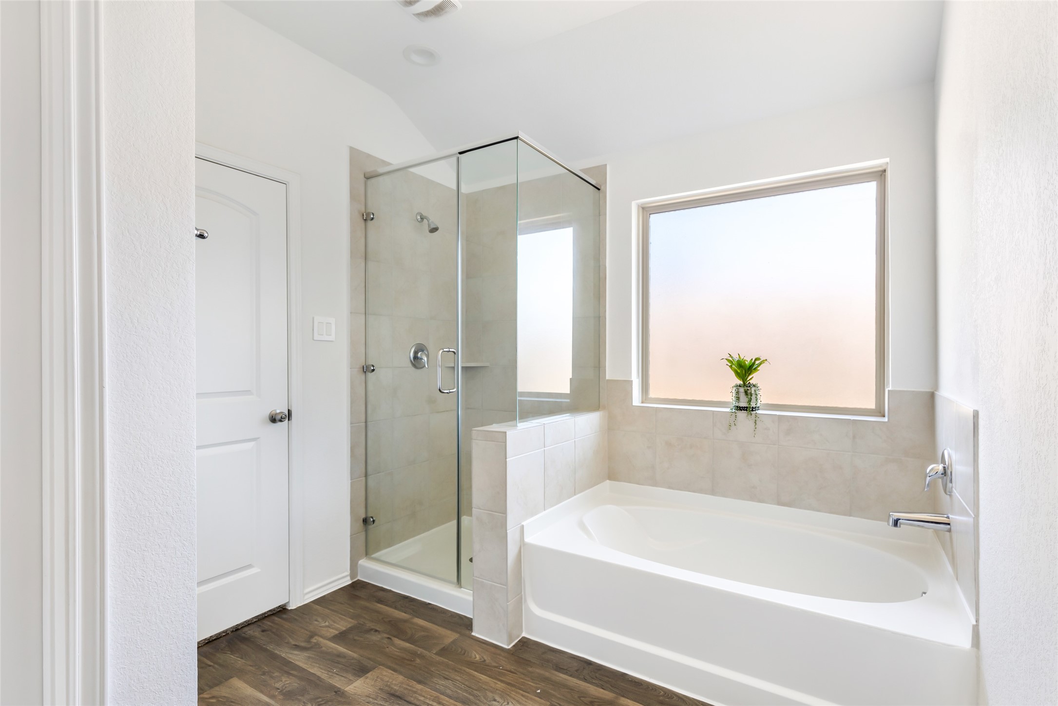 811 Republic Road New Caney, TX 77357 - Photo 37 of 37 This bathroom features a modern design with a glass-enclosed shower and a separate bathtub. The space is brightened by a large frosted window, allowing natural light while maintaining privacy. The room has neutral tones and wood-like flooring, creating a clean and inviting atmosphere.