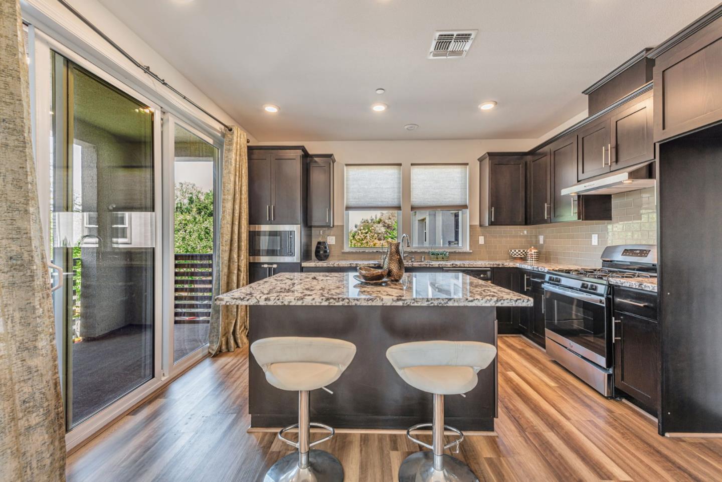 96 Zenith Common Fremont, CA 94539 - Photo 12 of 53 a kitchen with stainless steel appliances granite countertop a stove a refrigerator a kitchen island and chairs in it