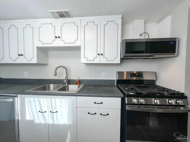 a kitchen with stainless steel appliances granite countertop a sink dishwasher a stove and a microwave oven with white cabinets