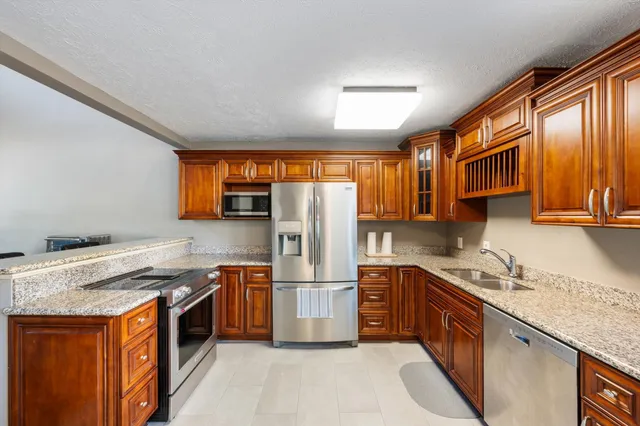 a kitchen with stainless steel appliances granite countertop a refrigerator a sink dishwasher a stove and white countertops with wooden floor