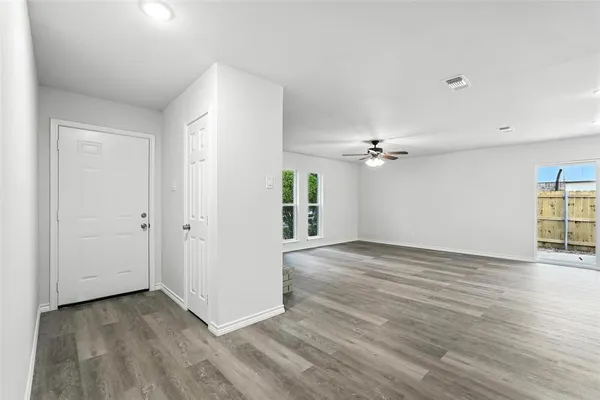 an empty room with wooden floor ceiling fan and windows