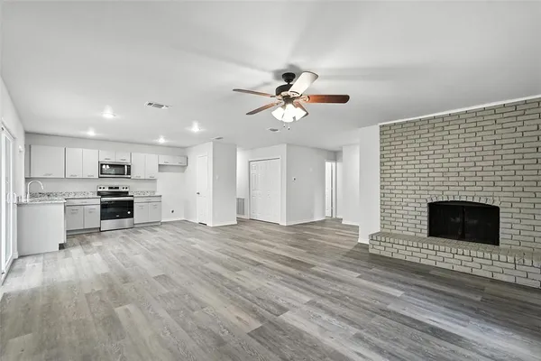 a view of an empty room with kitchen and fireplace