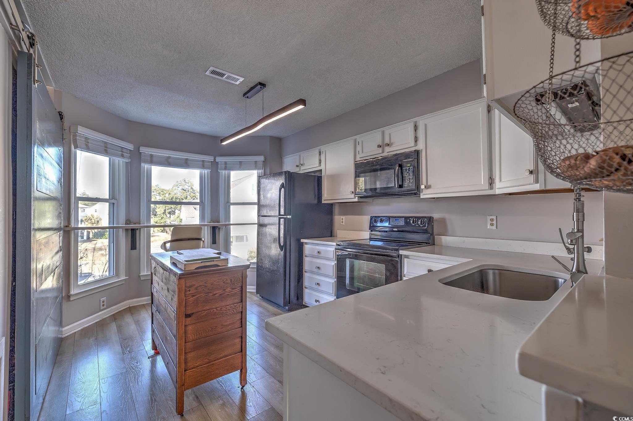 4999 Highway 17 Business, Unit 305 Murrells Inlet, SC 29576 - Photo 11 of 27 Kitchen with black appliances, white cabinetry, light wood-type flooring, a textured ceiling, and light stone counters