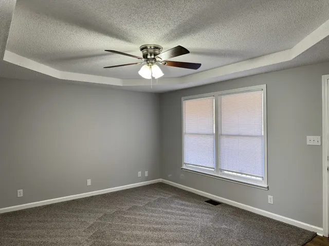 an empty room with chandelier fan and windows