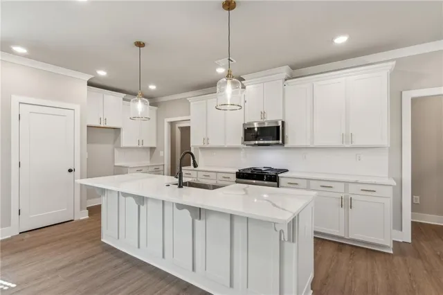 a kitchen with stainless steel appliances granite countertop a sink a stove a refrigerator and white cabinets with wooden floor