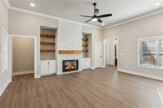 an empty room with windows a fireplace a ceiling fan and wooden floor