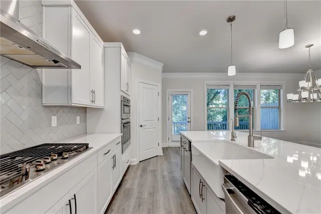 a kitchen with granite countertop a stove a sink a refrigerator and white cabinets with wooden floor