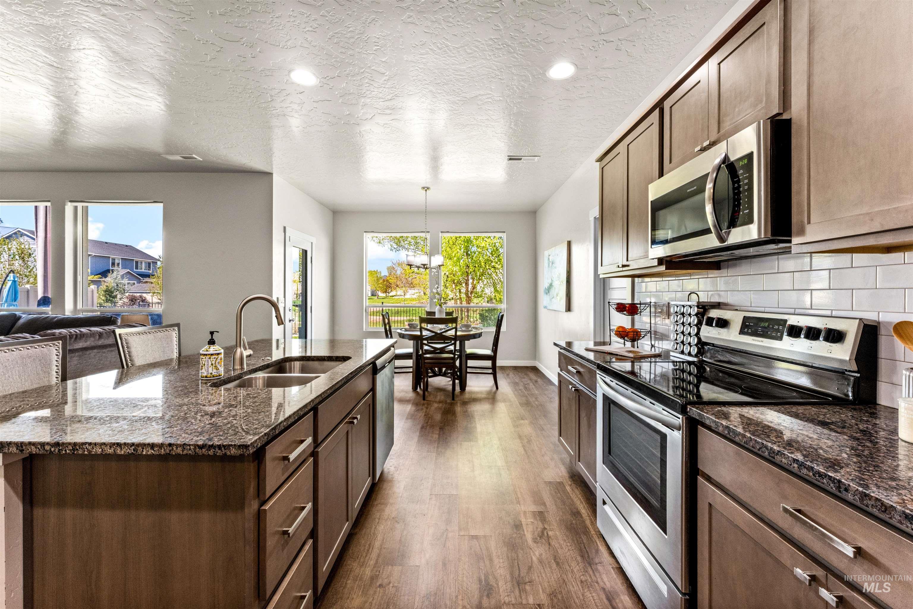 10890 West Sharpthorn Street Boise, ID 83709 - Photo 12 of 50 Open-concept kitchen featuring granite countertops, wood-finish flooring, stainless steel appliances, a subway tile backsplash, and recessed lighting