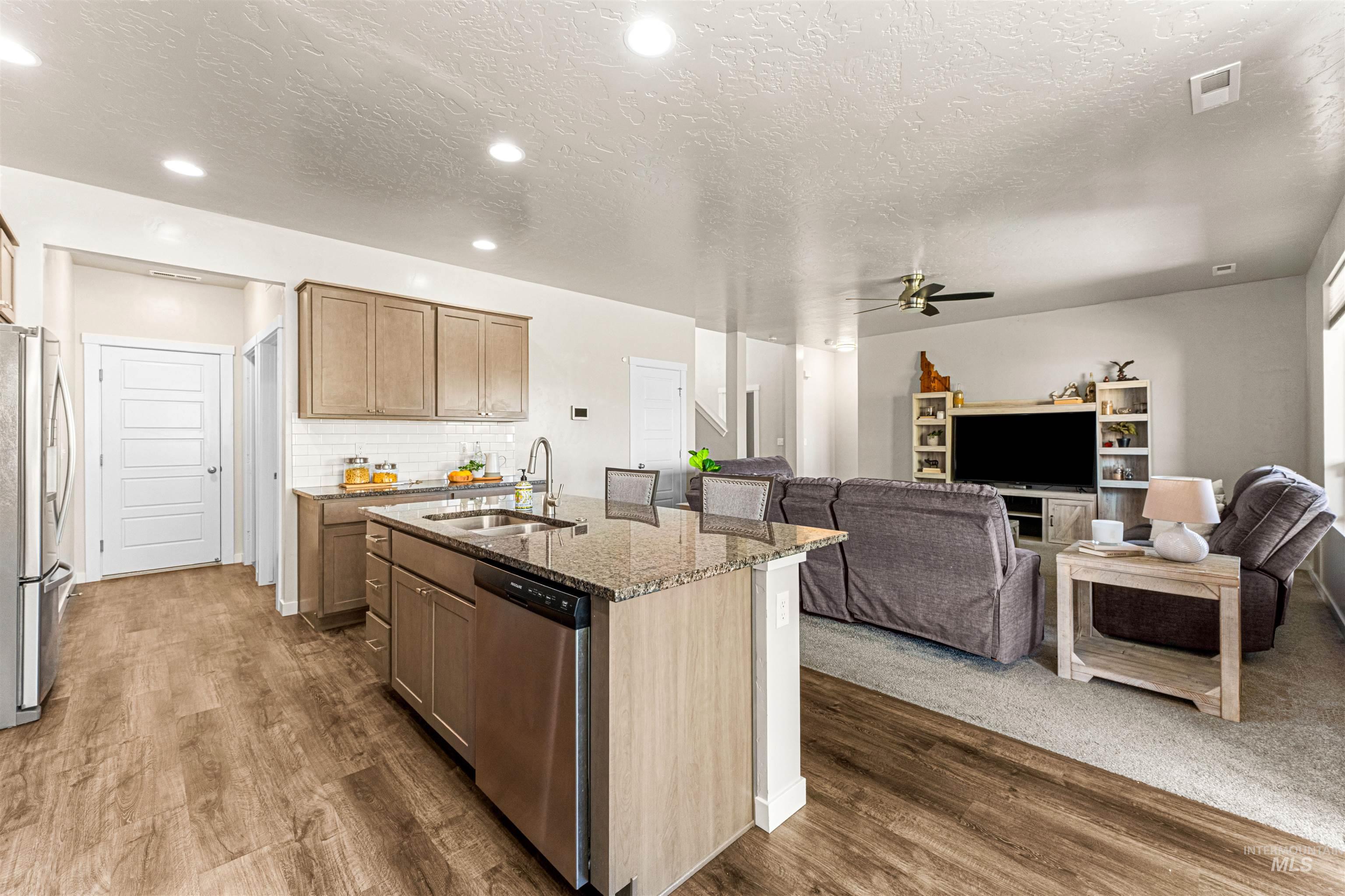 10890 West Sharpthorn Street Boise, ID 83709 - Photo 14 of 50 Open concept living space featuring a kitchen island with built-in sink and dishwasher, wood-finish flooring, recessed lighting, and a white subway tile backsplash