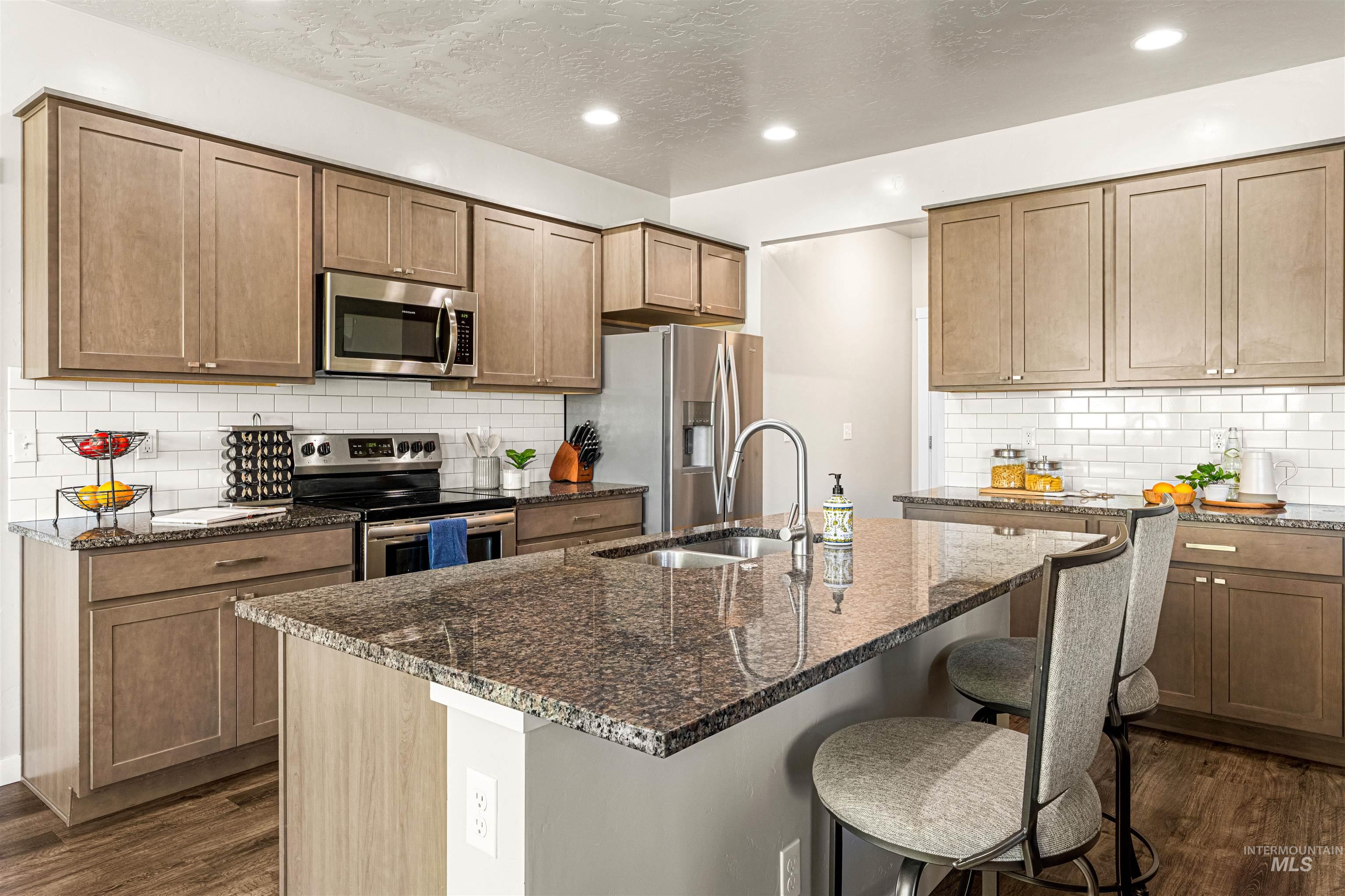 10890 West Sharpthorn Street Boise, ID 83709 - Photo 15 of 50 Modern kitchen featuring an expansive island with a granite countertop, stainless steel appliances, wood-finish cabinetry, a white subway tile backsplash, and recessed lighting