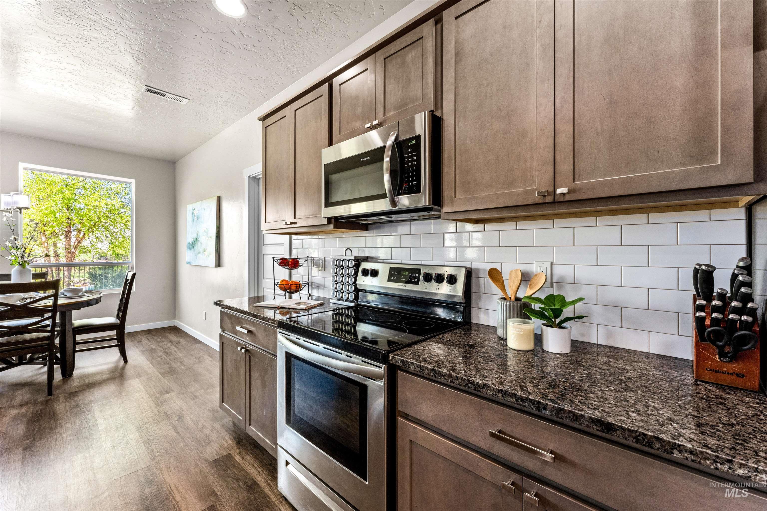 10890 West Sharpthorn Street Boise, ID 83709 - Photo 16 of 50 Kitchen featuring wood-finish flooring, stainless steel range and microwave, wood cabinetry, granite-style countertops, and a white subway tile backsplash