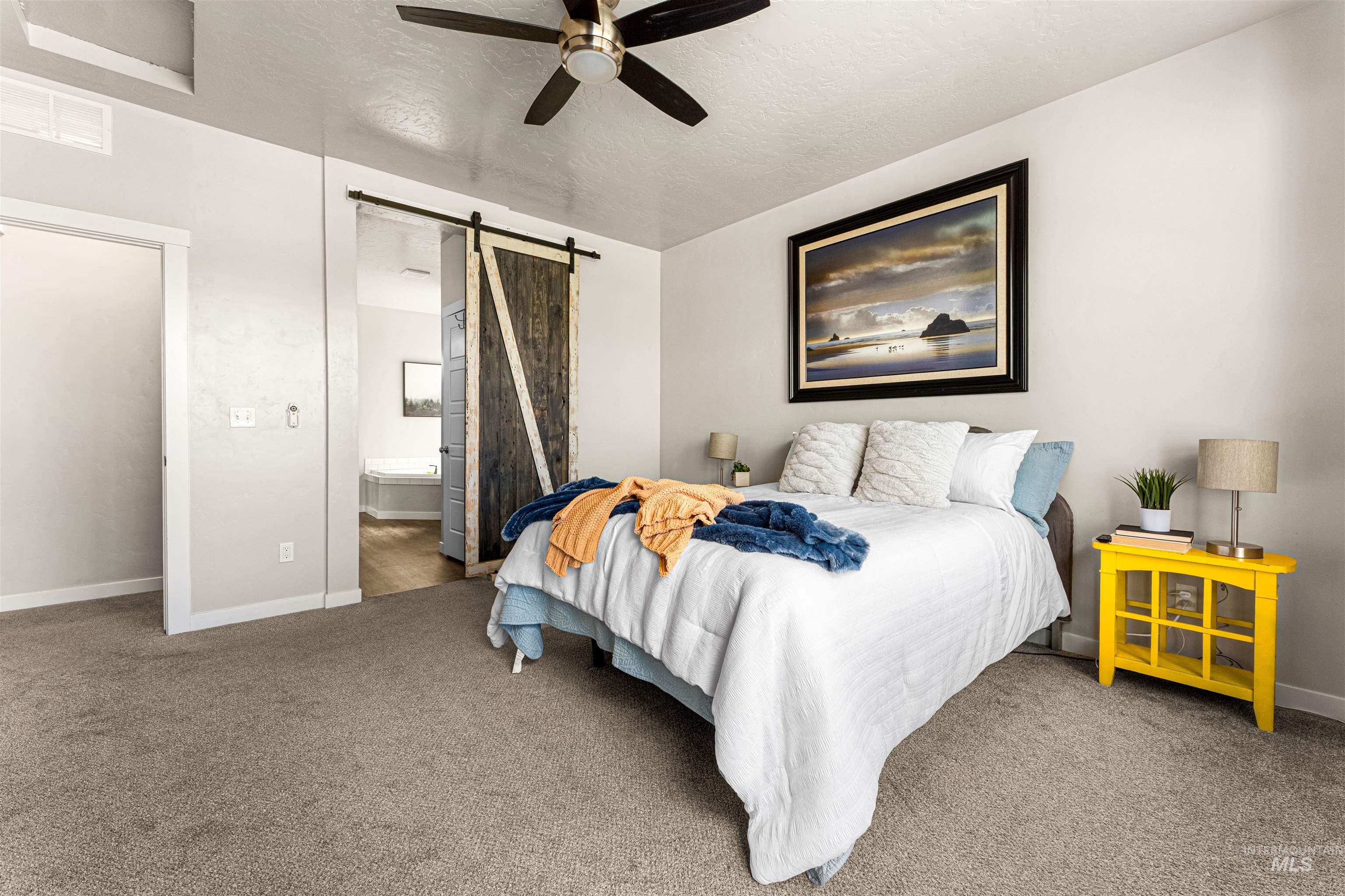 10890 West Sharpthorn Street Boise, ID 83709 - Photo 23 of 50 Carpeted bedroom featuring a contemporary ceiling fan, white trim, and a rustic barn door entry to a bathroom with a built-in tub