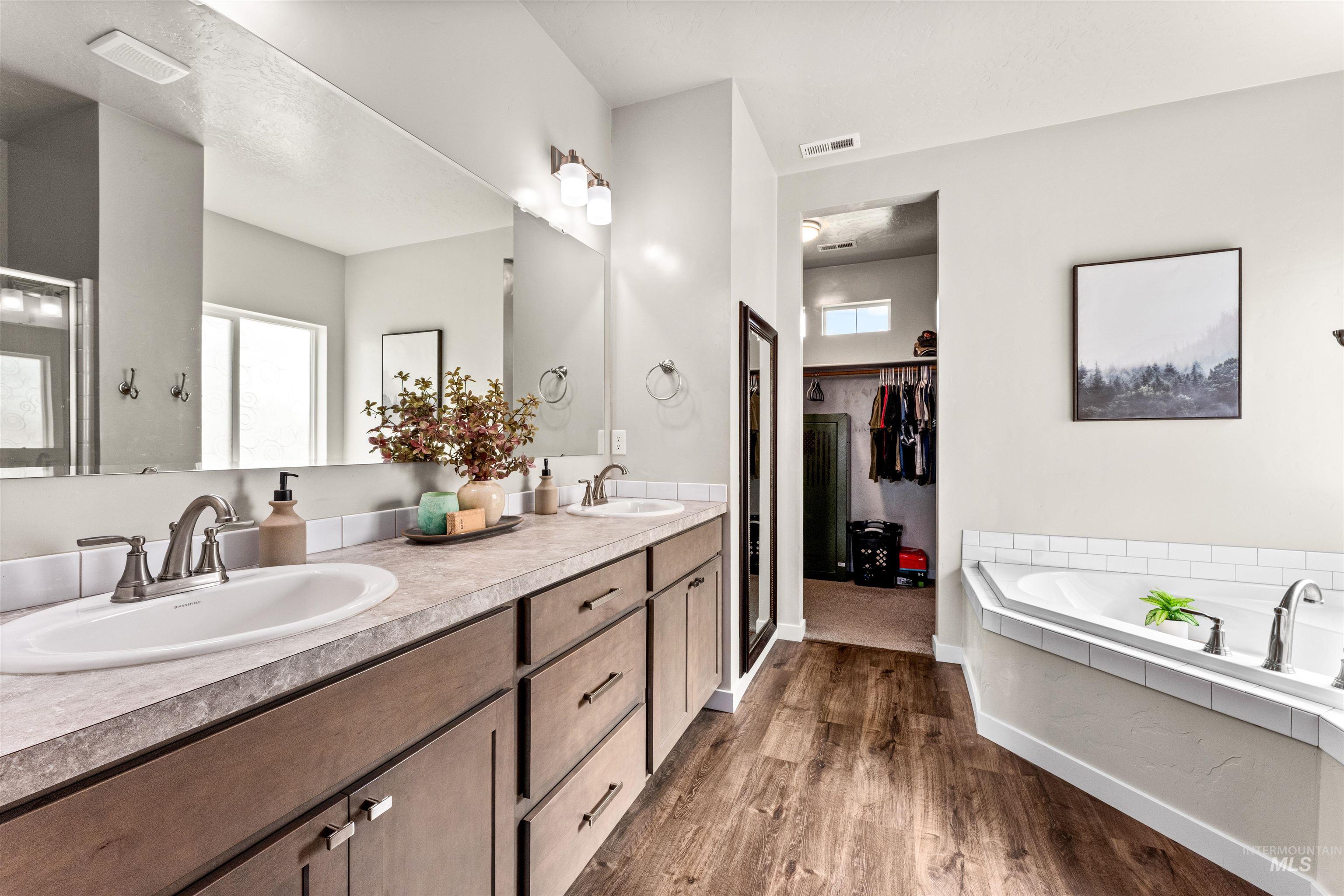 10890 West Sharpthorn Street Boise, ID 83709 - Photo 24 of 50 Spacious bathroom featuring a double vanity with wood-finish cabinetry, a large mirror, and a corner soaking tub with white subway tile surround