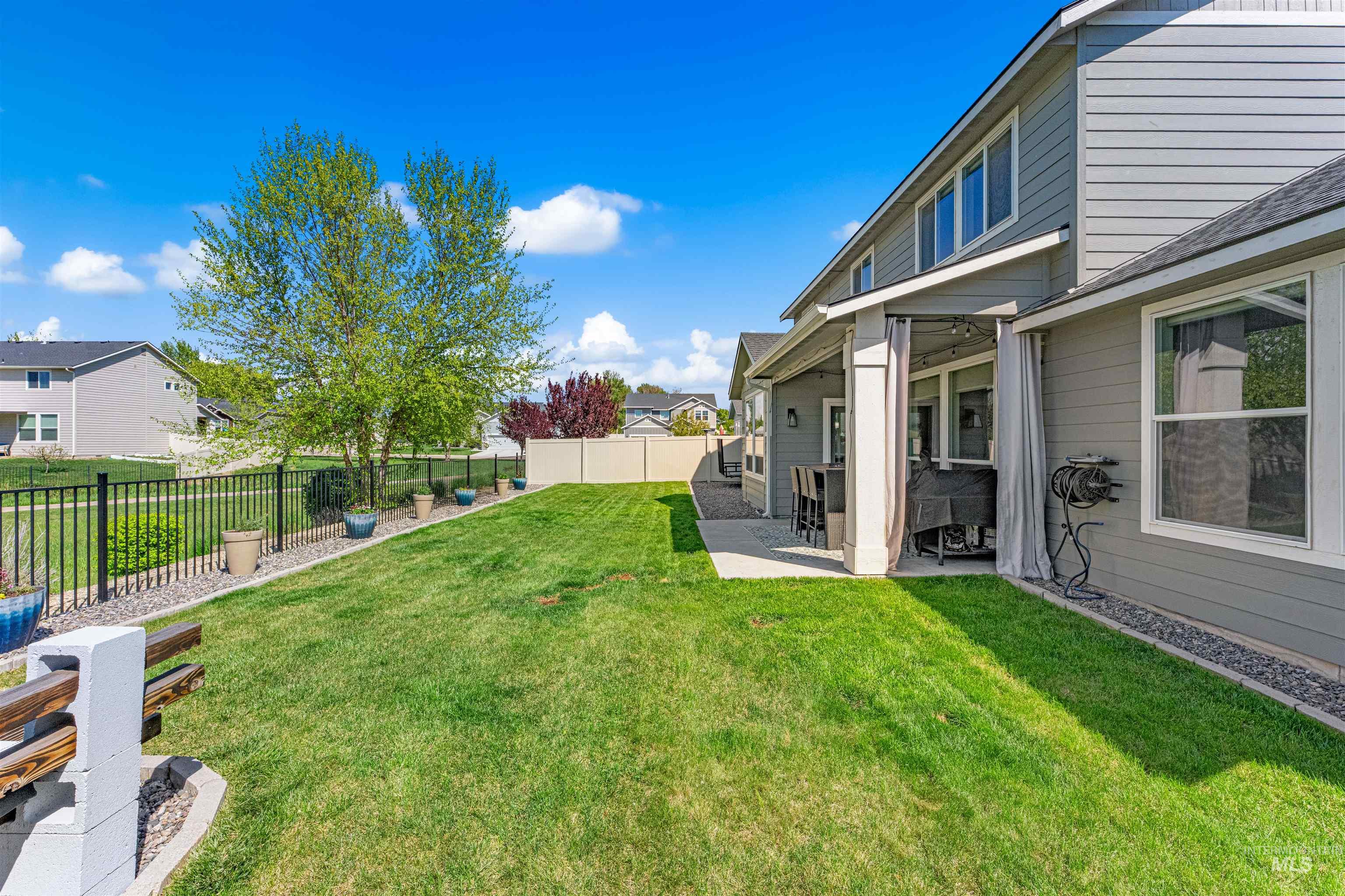 10890 West Sharpthorn Street Boise, ID 83709 - Photo 45 of 50 Expansive backyard featuring a large green lawn, covered patio, and a black metal fence