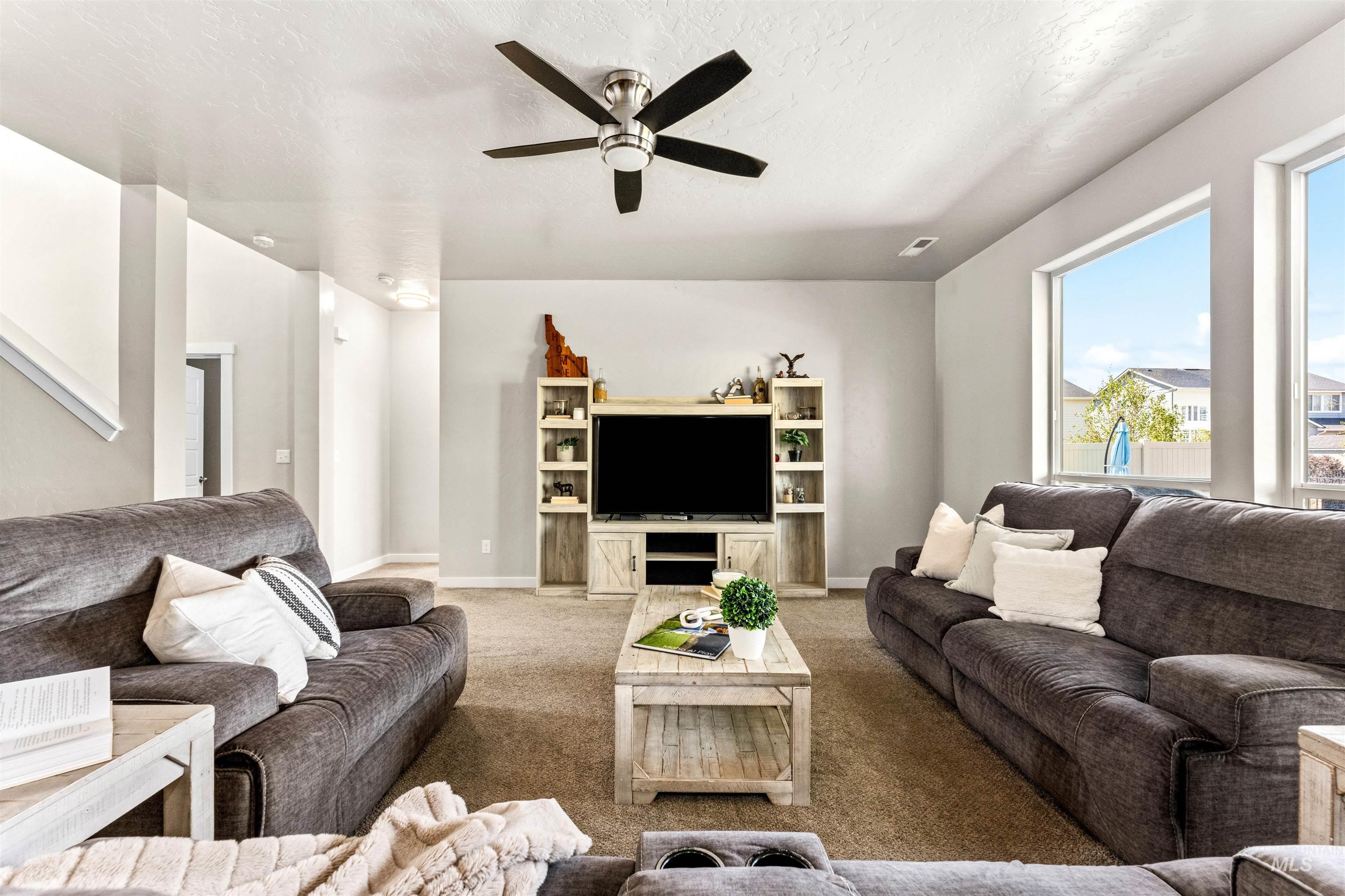 10890 West Sharpthorn Street Boise, ID 83709 - Photo 10 of 50 Spacious living area featuring neutral carpeting, a ceiling fan with integrated lighting, and multiple large windows