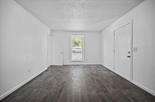 a view of an empty room with wooden floor and window