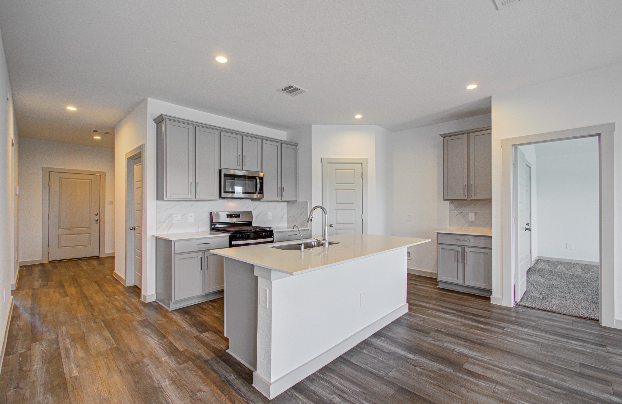7903 Wrangler Shack Lane Rosharon, TX 77583 - Photo 13 of 29 This modern kitchen boasts sleek grey cabinetry, stainless steel appliances, and a spacious island, all set in an open layout with wood-look flooring and recessed lighting, creating a bright, inviting space perfect for cooking and entertaining.