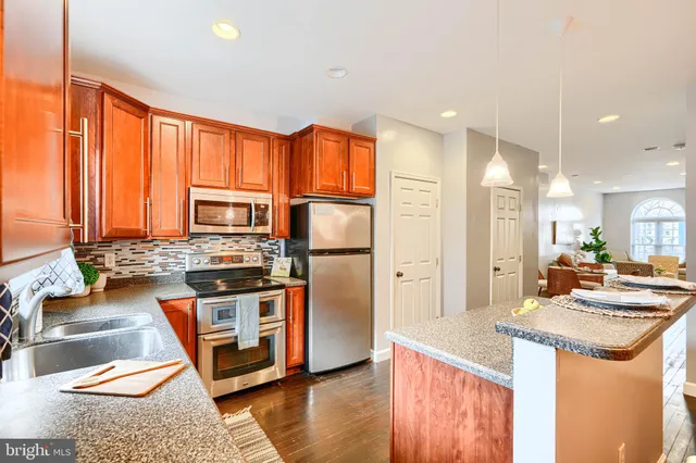 a kitchen with stainless steel appliances granite countertop a refrigerator a stove and a sink with wooden floor
