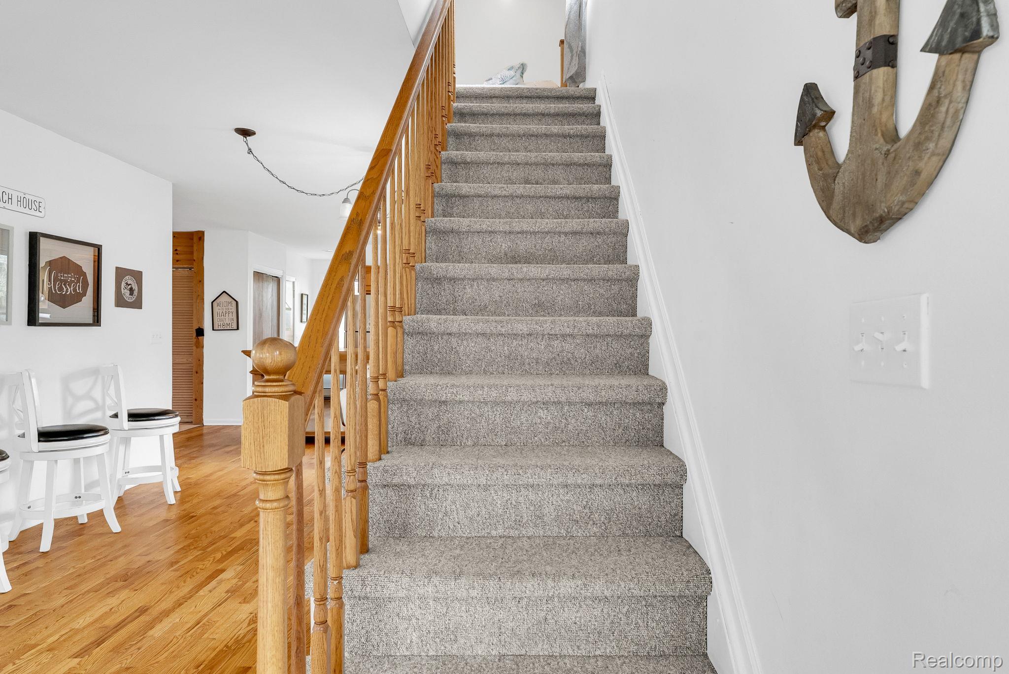 7489 Aspen Road Lexington, MI 48450 - Photo 39 of 62 Carpeted staircase with a wood handrail and balusters, accompanied by natural wood-finish flooring
