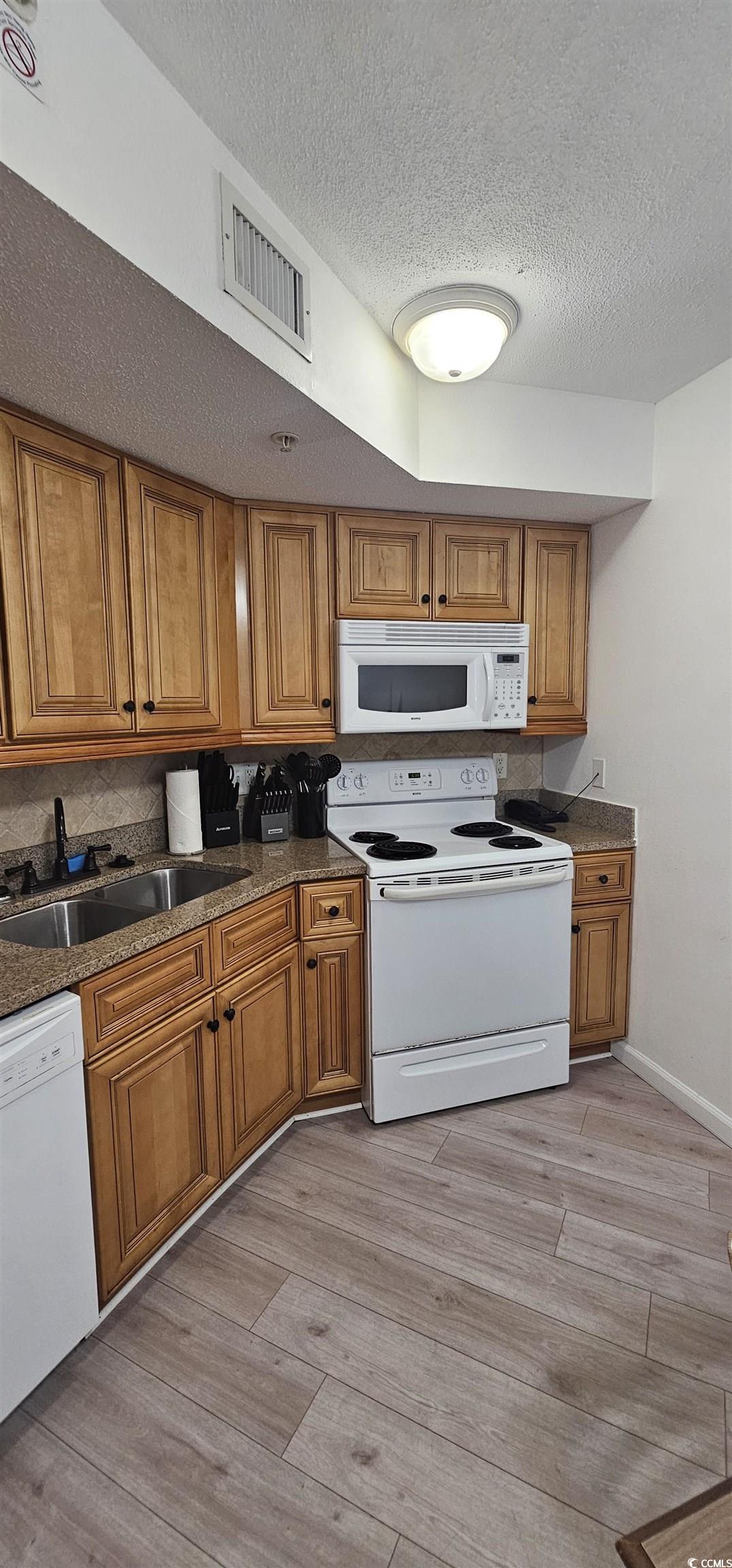 7100 North Ocean Boulevard, Unit 724 Myrtle Beach, SC 29572 - Photo 3 of 16 Kitchen featuring brown cabinets, white appliances, light wood-type flooring, dark stone countertops, and a textured ceiling