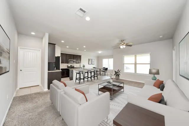 a living room with couches a coffee table and kitchen view with wooden floor