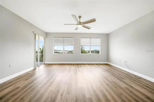 an empty room with wooden floor windows and ceiling fan