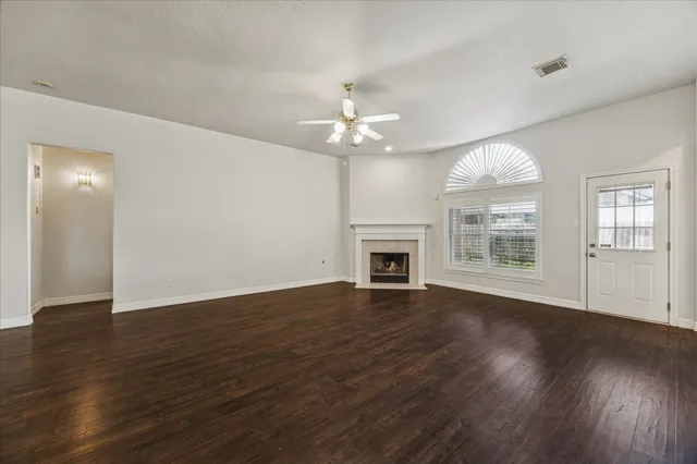 an empty room with wooden floor chandelier fan and windows