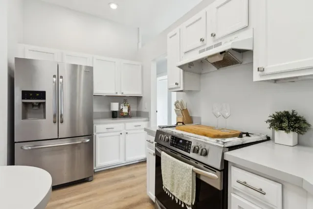 a kitchen with stainless steel appliances a refrigerator a stove a sink and white cabinets