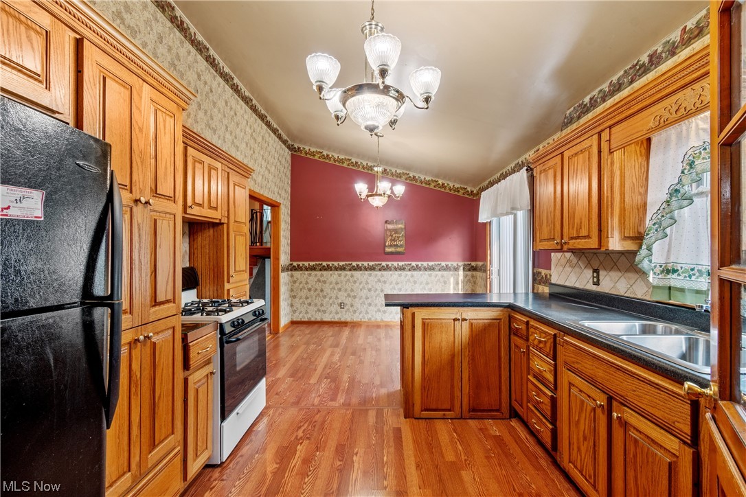 120 Lester Road New Franklin, OH 44319 - Photo 8 of 24 Kitchen featuring white gas range oven, a chandelier, dark countertops, black fridge, brown cabinets, backsplash, and light hardwood floors
