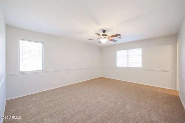 an empty room with windows and chandelier fan