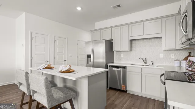 a kitchen with stainless steel appliances kitchen island a table chairs sink and cabinets