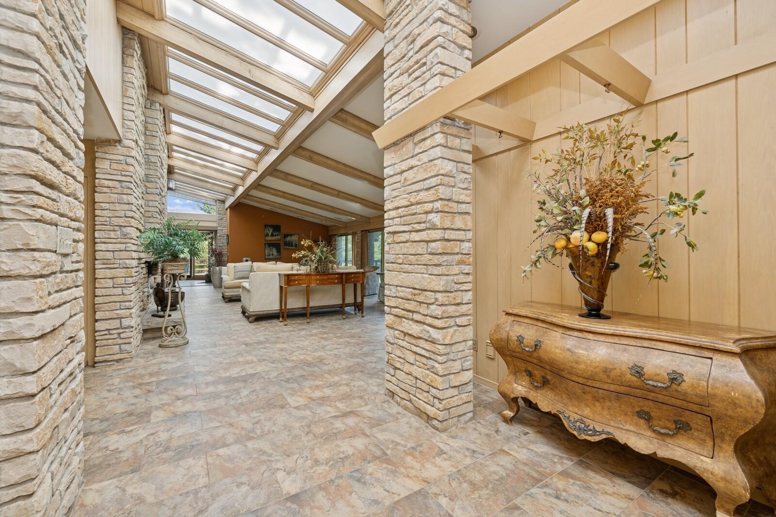 W1800 County Road B Bloomfield, WI 53128 - Photo 28 of 81 An open interior hallway with stone columns, tile flooring, and exposed beams creates a seamless flow between living spaces.