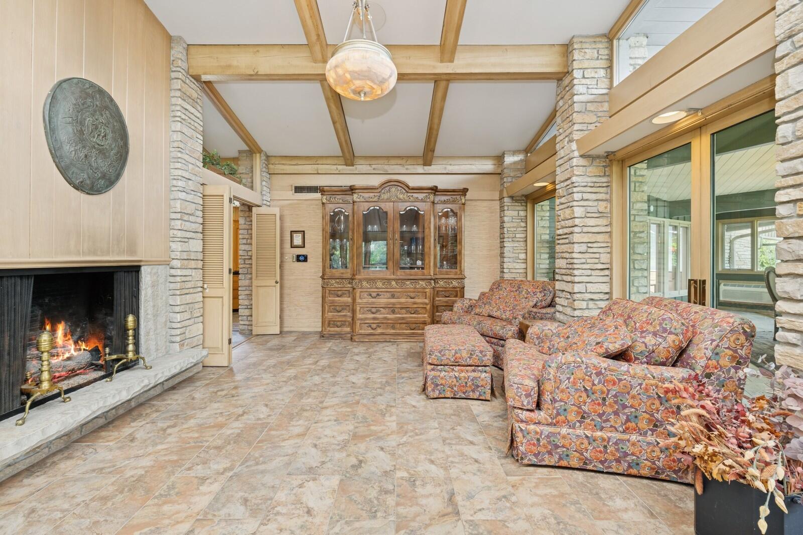 W1800 County Road B Bloomfield, WI 53128 - Photo 34 of 81 An inviting sitting area anchored by a stone fireplace, featuring exposed beams, tile flooring, and warm architectural details.