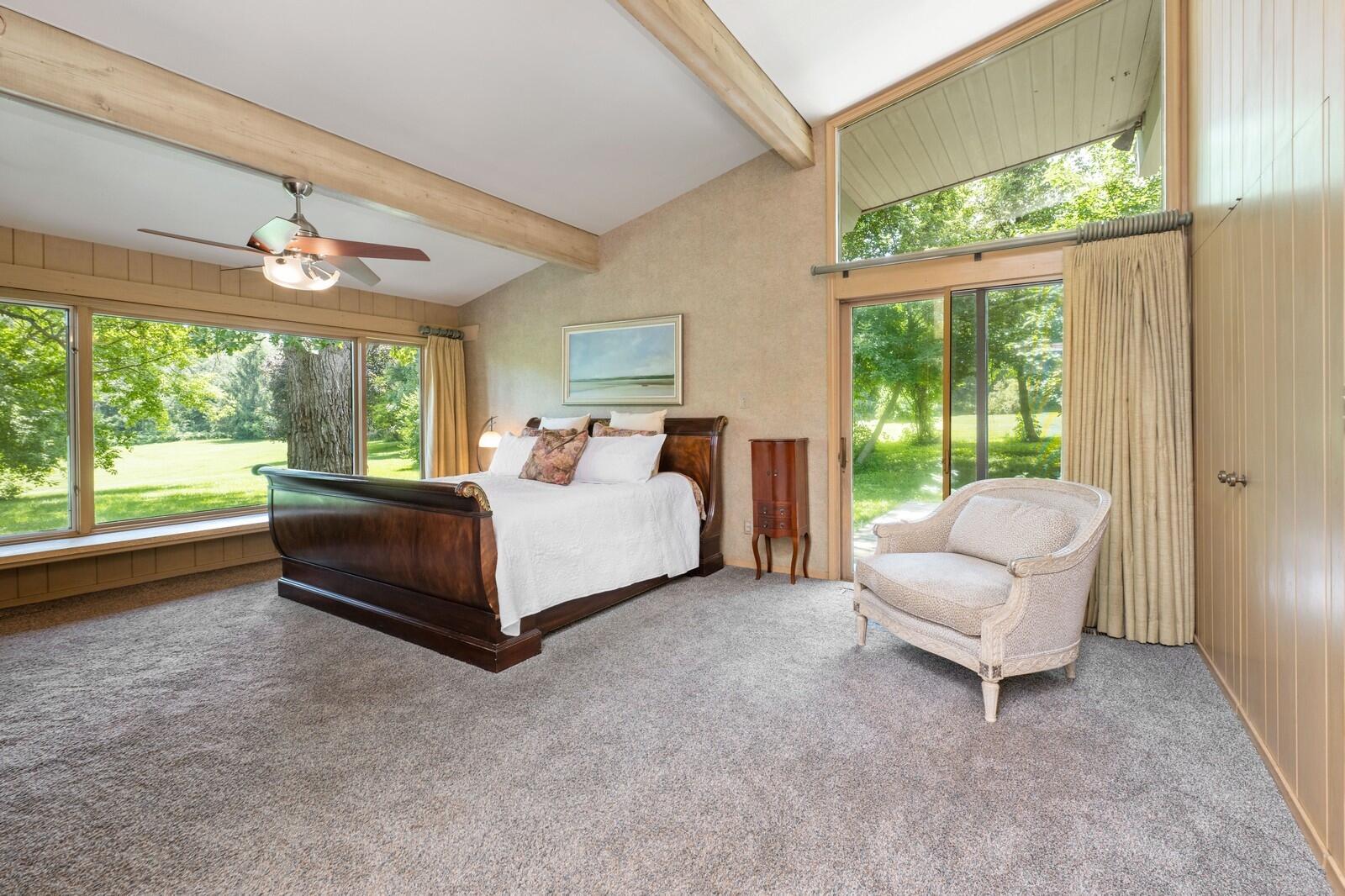 W1800 County Road B Bloomfield, WI 53128 - Photo 41 of 81 Spacious primary bedroom showcasing exposed ceiling beams, generous windows, and peaceful views of mature trees and lawn with access to private deck and hot tub.