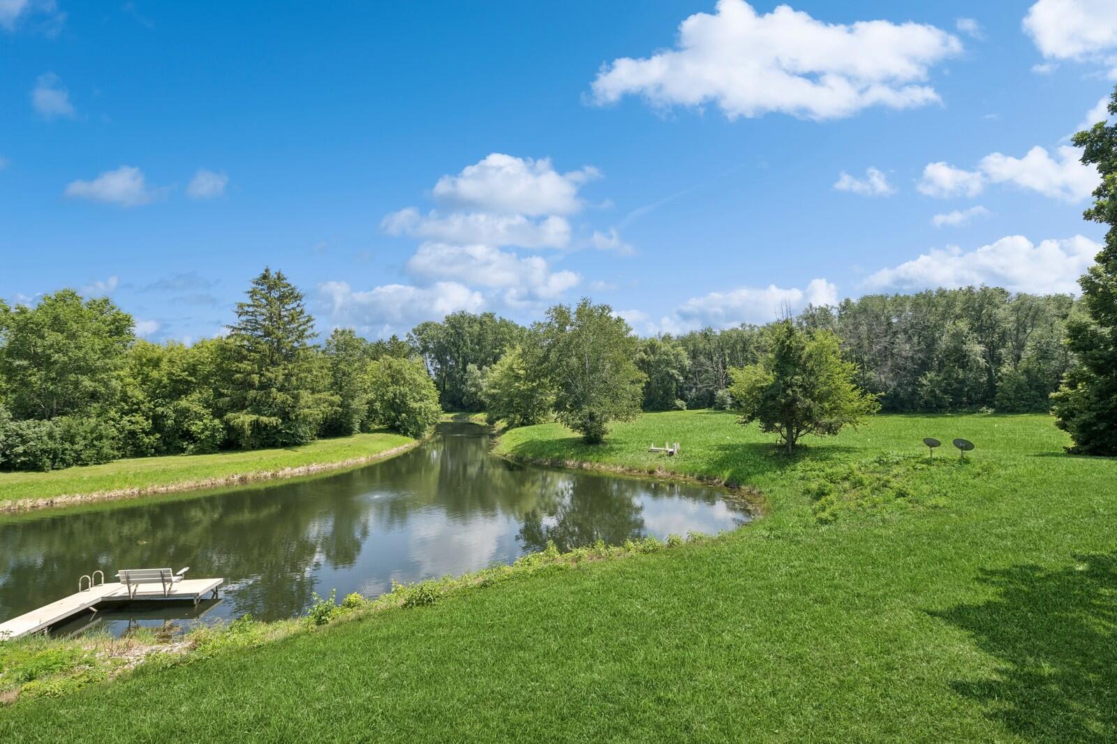 W1800 County Road B Bloomfield, WI 53128 - Photo 55 of 81 A scenic, spring-fed pond bordered by open lawn and mature trees, creating a peaceful natural focal point on the property.
