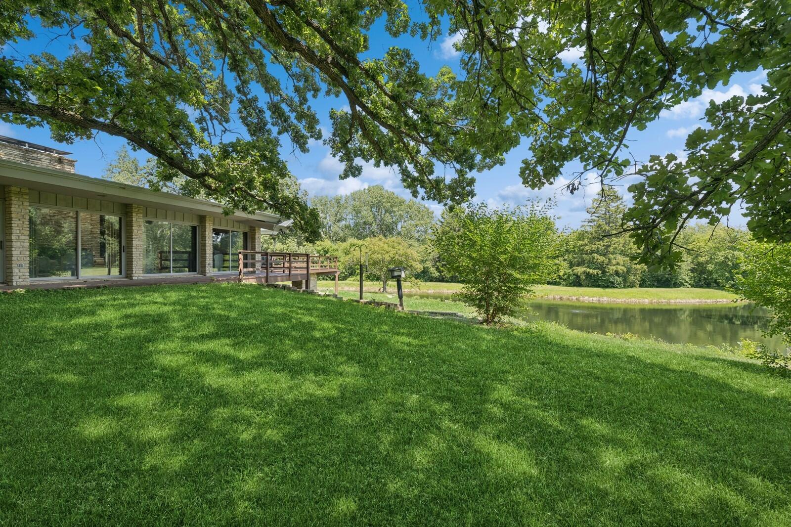 W1800 County Road B Bloomfield, WI 53128 - Photo 58 of 81 A tranquil backyard setting with mature trees, open lawn, and picturesque views of the spring-fed pond, offering a peaceful connection to the surrounding landscape.