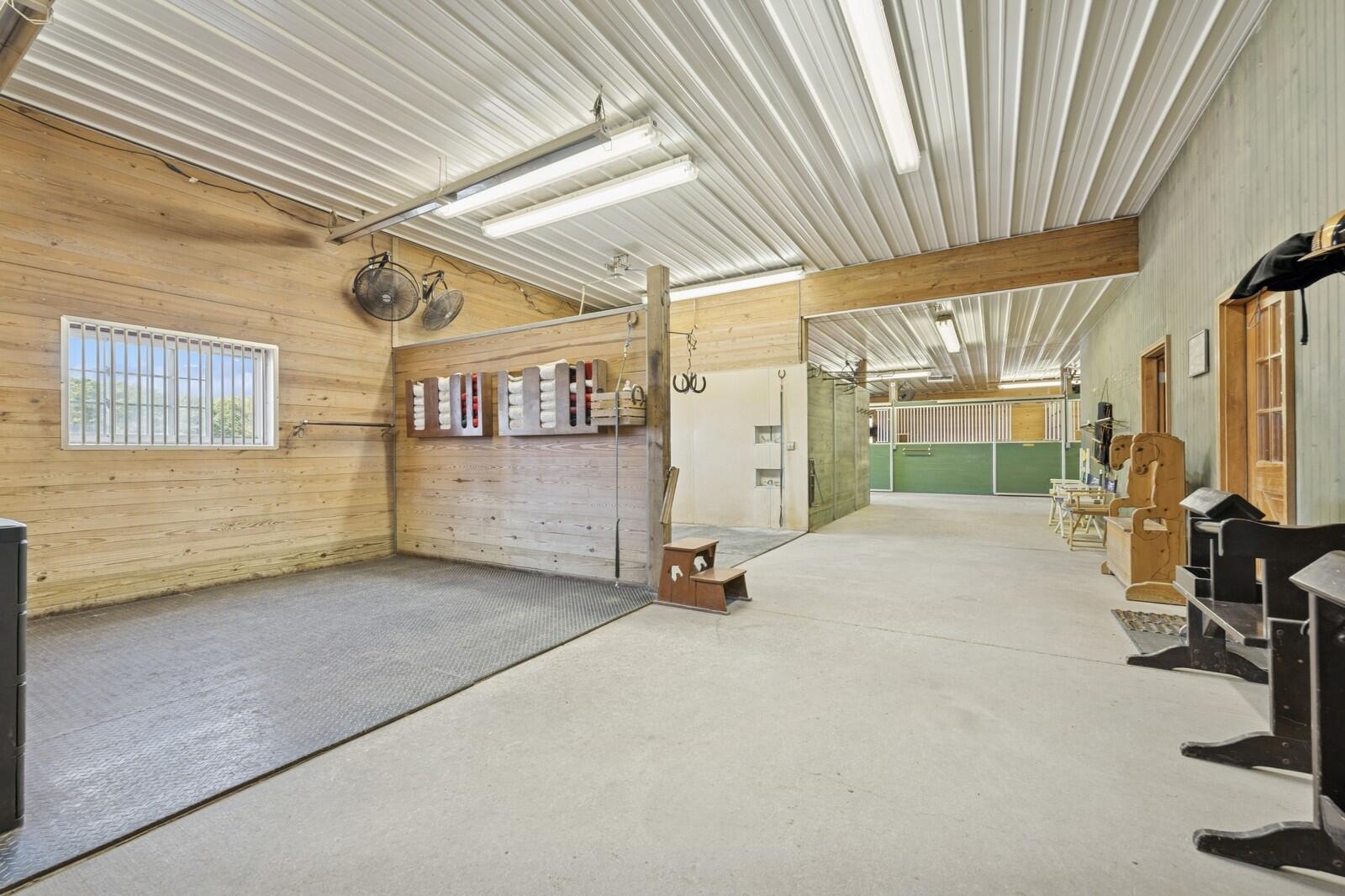 W1800 County Road B Bloomfield, WI 53128 - Photo 6 of 81 Spacious prep area with rubber mat surface, wood-paneled walls, and convenient access to nearby stalls and tack storage.