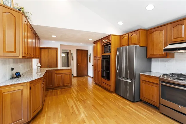 a kitchen with stainless steel appliances granite countertop a refrigerator a sink dishwasher and wooden cabinets with wooden floor